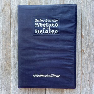 May include: A dark blue book with the title "The Love Sonnets of Abelard and Heloise" in white lettering on the front cover. The author's name, "Ella Wheeler Wilcox", is printed in white lettering at the bottom of the cover.