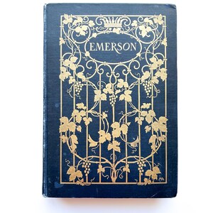 May include: A vintage book with a navy blue cover and gold leaf design. The cover features the name "EMERSON" in a gold oval, surrounded by a gold vine and grape motif. The book is set against a white background.