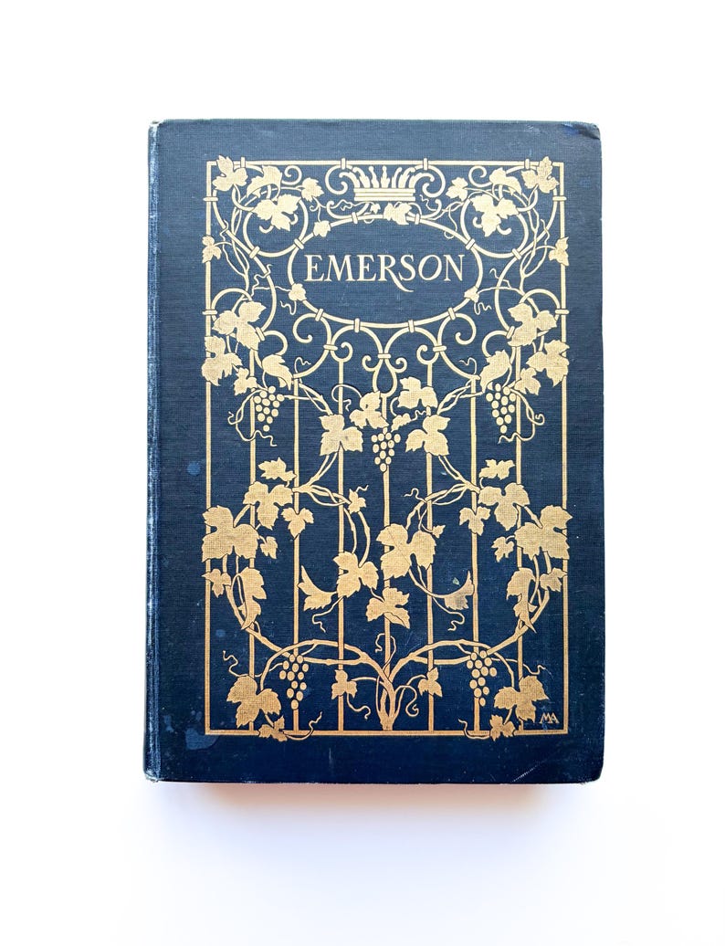 May include: A vintage book with a navy blue cover and gold leaf design. The cover features the name "EMERSON" in a gold oval, surrounded by a gold vine and grape motif. The book is set against a white background.