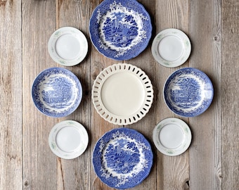 May include: A collection of seven blue and white patterned ceramic plates with a white plate in the center. The plates are arranged in a circle on a wooden surface.