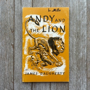 May include: A yellow book cover with black illustrations of a boy, a lion, and two dogs. The title is "Andy and the Lion" by James Daugherty. The book cover also includes the text "b. Mills".