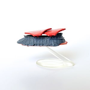 May include: A red and gray toy spaceship with a clear plastic stand. The spaceship has a rounded body and two red wings.