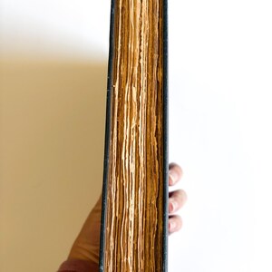 May include: A thick, antique book with aged, yellowed pages and a dark blue cover. The book's spine is visible, revealing the worn edges of the pages. The book is held by a person, with a white background.
