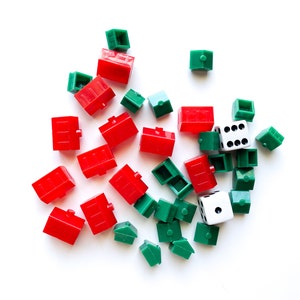 May include: A collection of red and green plastic houses and a white die with black dots. The houses are small and have a simple design. The die is a standard six-sided die.