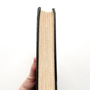 Puede incluir: Primer plano del lomo de un libro de tapa dura con una cubierta negra y p&aacute;ginas de color crema.