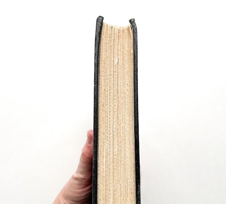 Puede incluir: Primer plano del lomo de un libro de tapa dura con una cubierta negra y p&aacute;ginas de color crema.