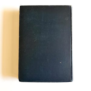 May include: A rectangular, black book with a slightly textured cover. The book is closed and viewed from the top, showing the spine and edges. The cover has minor wear and tear.