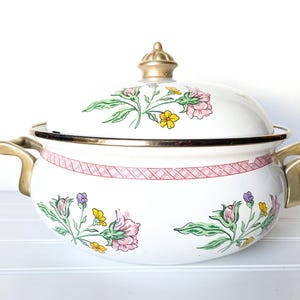 May include: White enamel pot with a floral design and gold accents. The pot has a lid with a gold knob and a pink and white checkered pattern around the rim.