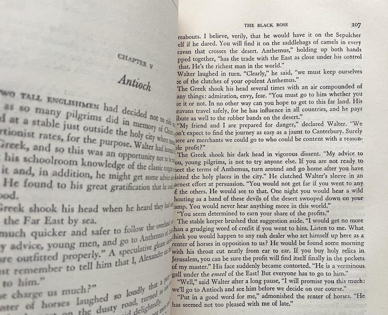 Puede incluir: Una p&aacute;gina de un libro antiguo titulado "La Rosa Negra" con texto sobre un viaje al Este. El texto describe a un mercader llamado Anthemus que controla el comercio con el Este y es conocido por sus caravanas.