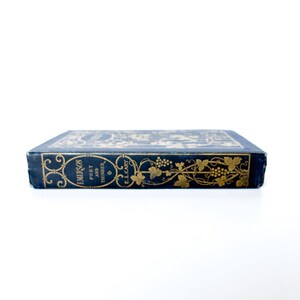 May include: A vintage book with a dark blue cover and gold embossed lettering and floral designs. The book's spine features the title "Emerson Poet and Thinker" and the author's name, E.L. Cary.
