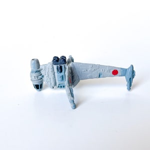 May include: A gray and blue toy spaceship with a red circle on the wing. The spaceship has a detailed design and is made of plastic.