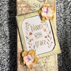 May include: A rustic wooden sign with a distressed brick background and a vintage butterfly image. The sign features a white frame with a floral design and the text "bloom with grace".