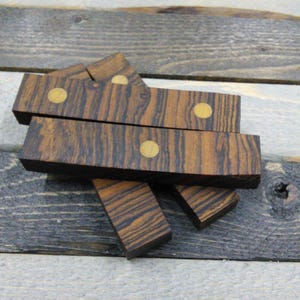 May include: Several rectangular wooden blocks with a dark brown and black striped pattern. Each block has a small, round, gold-colored accent. The blocks are arranged on a light gray and dark gray wooden surface.