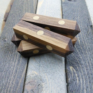 May include: A stack of four wooden objects with a geometric design. Each piece is a dark brown color with lighter brown stripes and inlaid with three small, round, light-colored accents. The objects are arranged on a weathered wooden surface.