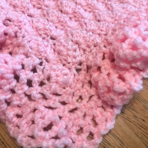 May include: A pink crocheted baby blanket with a delicate, lacy pattern.