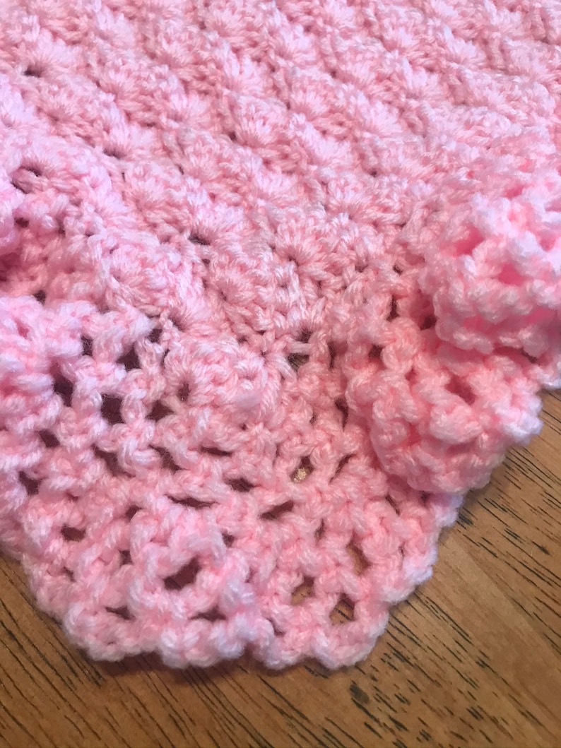 May include: A pink crocheted baby blanket with a delicate, lacy pattern.