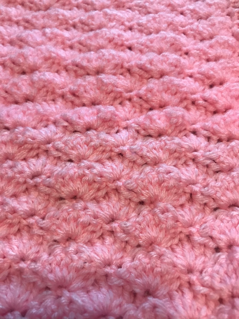 May include: A close-up of a pink crocheted blanket with a textured, woven pattern.