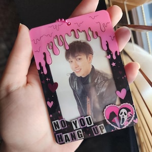 May include: Pink and black photo card with a dripping pink border. The card features a photo of a person with black hair and a black leather jacket. The text "NO YOU HANG UP" is printed on the card in black and pink.