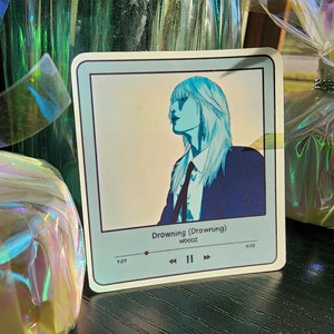 May include: A blue and white sticker with a stylized image of a person with long hair and a tie. The sticker has a music player interface with the text "Drowning (Drowning) WOOZ 1:01 4:05"