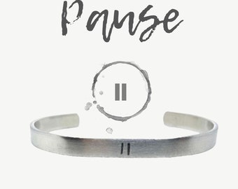 May include: A silver bracelet with the word "Pause" and a pause symbol engraved on it.