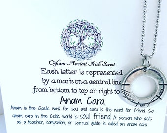 May include: A silver-colored pendant necklace with a circular pendant featuring etched lines. The pendant hangs on a ball chain. The background includes text about Ogham Ancient Irish Script and the words "Anam Cara".