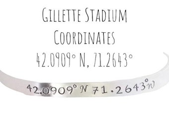 May include: A silver bracelet with the words "Gillette Stadium Coordinates 42.0909° N, 71.2643°" engraved on it.