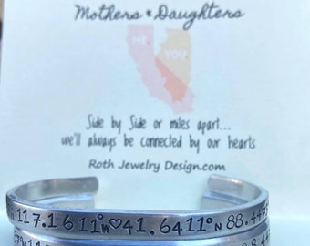 May include: Two silver bracelets with engraved coordinates and a heart symbol. The bracelets are stacked on top of each other. The text on the bracelets reads "117.1611°W 41.6411°N 88.4475" and "117.1611°W 41.6411°N 88.4475".