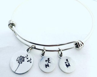 May include: Silver bangle bracelet with three charms. The charms are round and feature a dandelion, the letter "N", and the letter "M".
