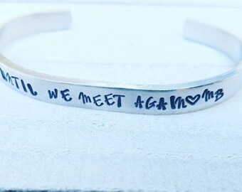 May include: Silver bangle bracelet with the inscription "Until we meet again" and a heart symbol.