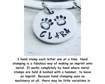 May include: A silver charm bracelet with a silver charm featuring two paw prints and the name "CLARA" hand-stamped on it.