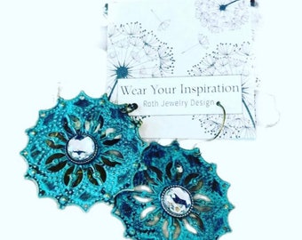 May include: Teal blue earrings with a filigree design and a clear rhinestone in the center. The earrings are on a white card with the text "Wear Your Inspiration Roth Jewelry Design".