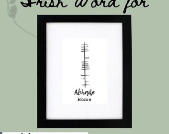 May include: A framed print with the words "Irish Word for" in cursive script at the top. The print features a black and white design with the word "Abhaile" and "Home" below. The frame is black.