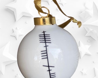 May include: White Christmas bauble with a gold top and a black and white rune symbol. The bauble has a gold ribbon.