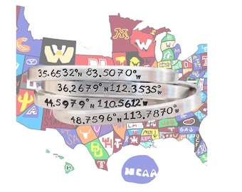 May include: Silver bracelets engraved with latitude and longitude coordinates are stacked in front of a colorful map of the United States. The bracelets have the following coordinates: 35.6532°N 83.5070°W, 36.2679°N 112.3535°W, 44.5979°N 110.5612°W, and 48.7596°N 113.7870°W.