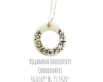 May include: A silver pendant necklace featuring a circular charm with stamped coordinates and the text "Villanova University Coordinates". The coordinates are 40.0369° N, 75.3426°.