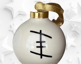May include: White ceramic Christmas bauble with a gold top and a black geometric design. The bauble has a gold string for hanging.