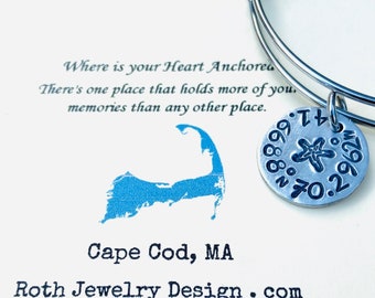May include: Silver charm bracelet with a charm shaped like Cape Cod, Massachusetts. The charm has the text "Where is your Heart Anchored? There's one place that holds more of you. memories than any other place." and "Cape Cod, MA". The charm also has a starfish and the text "88N702". The bracelet is on a white background. Roth Jewelry Design.com