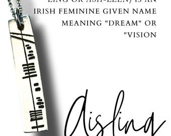 May include: A silver necklace with a rectangular pendant. The pendant has black markings and the name "Aisling" in cursive. Text on the image explains the name's meaning and pronunciation.