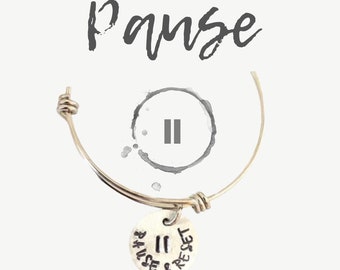 May include: Silver charm bracelet with a silver charm that says "Pause & Reset" with a pause symbol on it. The bracelet is on a white background.