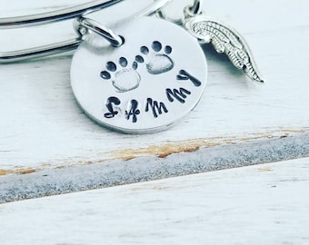 May include: Silver charm bracelet with a round charm featuring two paw prints and the name "Sammy" engraved on it. A small angel wing charm hangs from the bracelet.