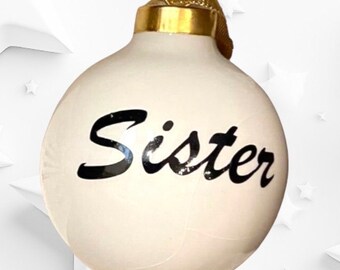 May include: White Christmas ornament with a gold top and the word "Sister" written in black cursive.