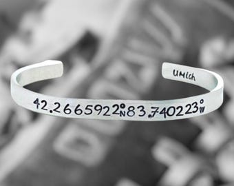 May include: Silver bracelet engraved with the coordinates 42.2665922°N 83.740223°W. The bracelet also has the text "UMich" engraved on it.