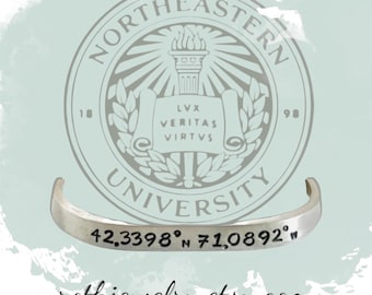 May include: Silver bracelet with the Northeastern University logo and coordinates 42.3398° N 71.0892° W engraved on it. The logo features a torch, scrolls, and the words "Lux Veritas Virtus" and "Northeastern University 1898".