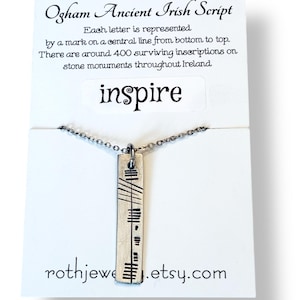May include: A silver necklace with a rectangular pendant, engraved with lines and dashes, hanging from a fine chain. The pendant is presented on a white card with the word "inspire" and text about Ogham Ancient Irish Script. The Etsy shop URL is visible.