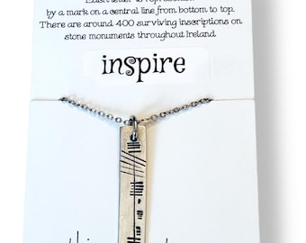 May include: A silver-toned necklace with a rectangular pendant featuring etched lines and dashes, suspended from a delicate chain. The pendant is displayed on a white card with the word "inspire" and text about Ogham Ancient Irish Script. The Etsy shop URL is visible.