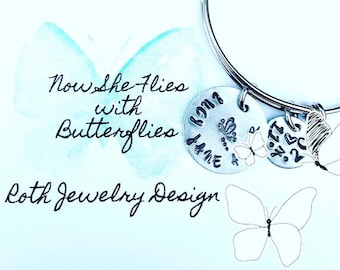 May include: Silver charm bracelet with a butterfly charm and two engraved discs. The larger disc reads "Now she flies with butterflies" and the smaller disc reads "1971-2022".