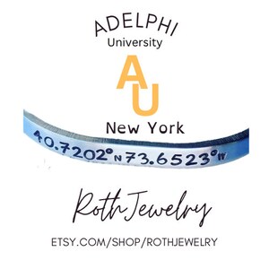 May include: A silver-colored bracelet with engraved coordinates and the text "40.7202°N 73.6523°W". The bracelet is curved and features the text "ADELPHI University" and "New York". The shop name "Roth Jewelry" is also visible.