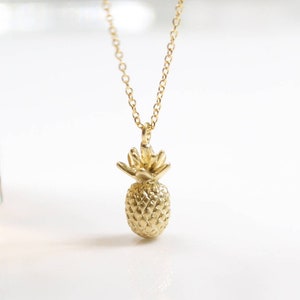 May include: A gold pineapple pendant necklace. The pineapple is detailed with a textured surface and a leafy crown.