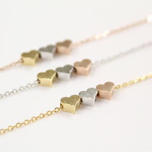 Op de afbeelding: Een delicate gouden ketting met een reeks kleine hartbedels in zilver, goud en rosé goud.