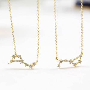 Può includere: Due collane d'oro con un designo a costellazione. Ogni collana presenta una catena delicata e un ciondolo a forma di costellazione con piccole pietre trasparenti.